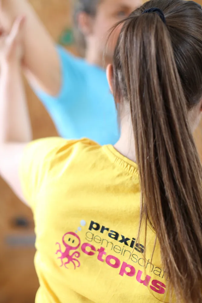 physiotherapie-graz-schulter-übung-mit-patientin Physio mit Logo am T-Shirt Terminvereinbarung